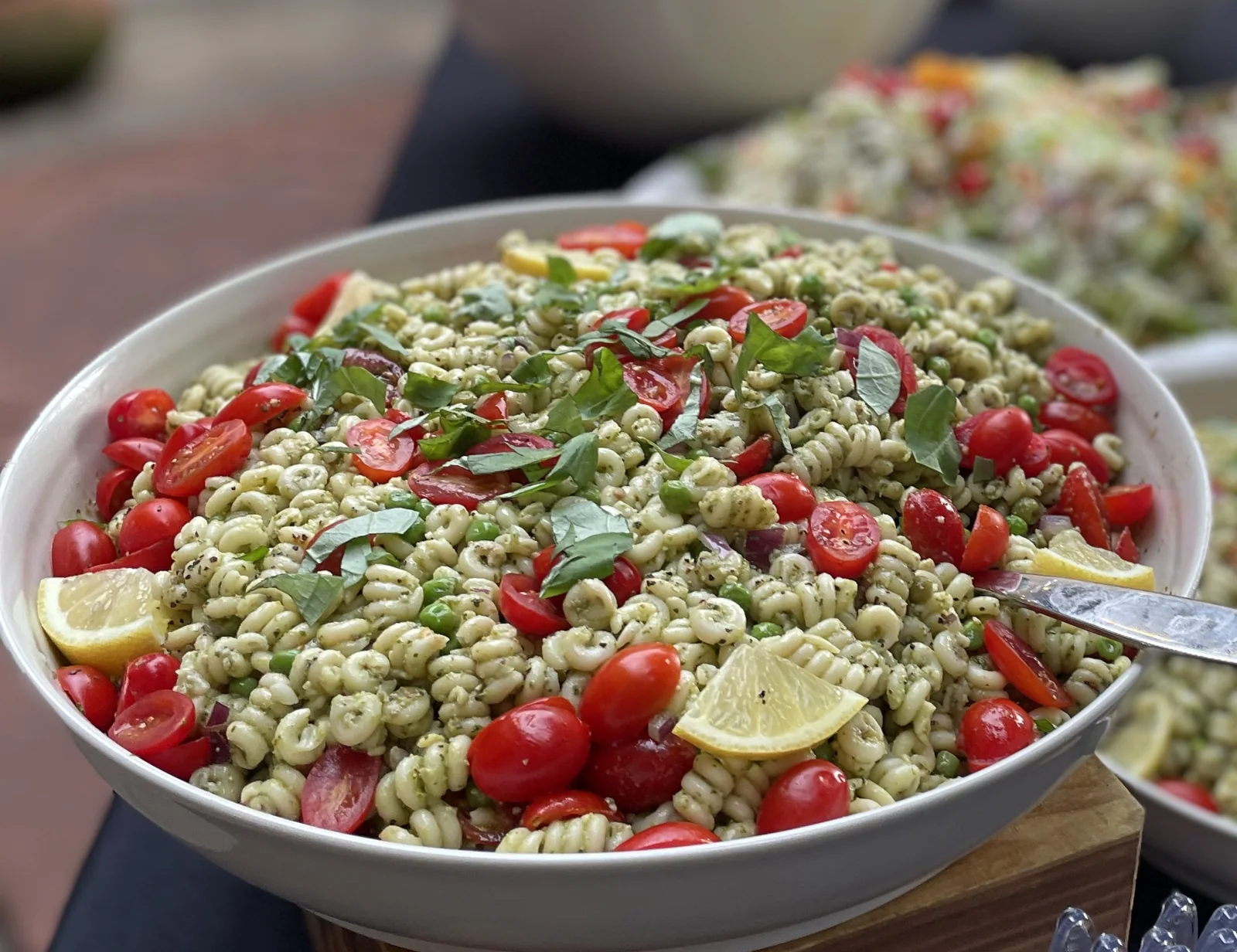 A bowl of pesto rotini salad with cherry tomatoes, peas, basil and lemon — one of the salads that comes in the bag