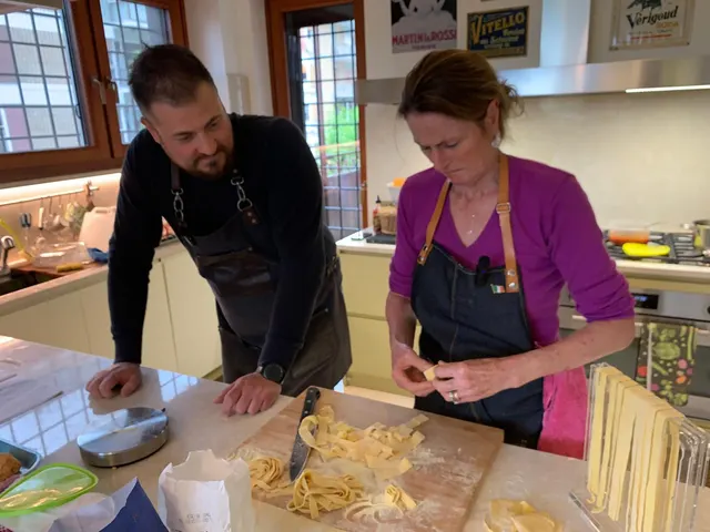 Chef Mylene and a fellow cook cutting fresh tagliatelle by hand on a wooden board in the kitchen
