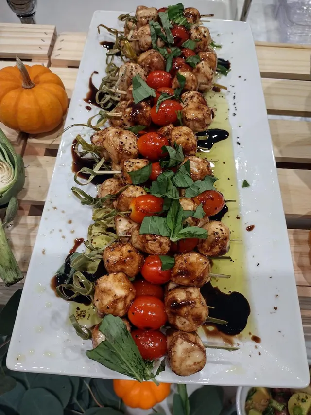A long platter of grilled chicken and cherry tomato skewers with basil and balsamic glaze, mini pumpkins alongside