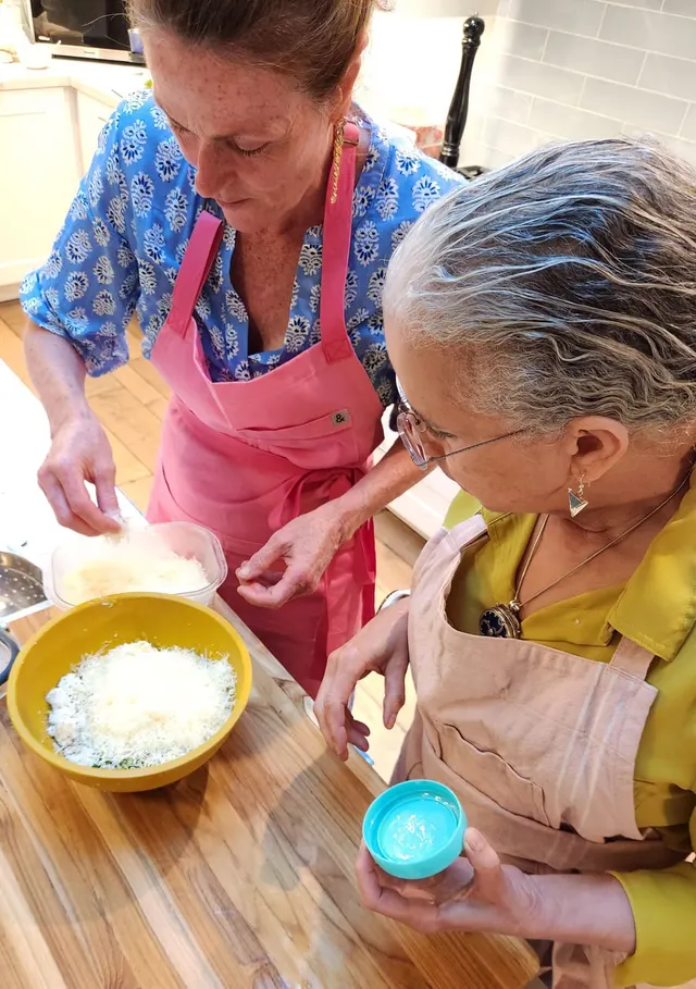 Chef Mylene in her pink apron grating parmesan into a bowl with a guest during a cooking session