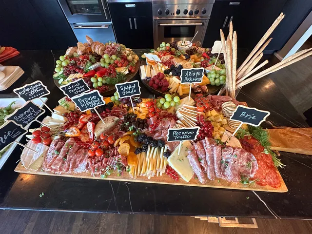 A grazing table of cured meats, cheeses, grapes and berries with chalkboard labels for brie, smoked gouda, asiago and pecorino truffle