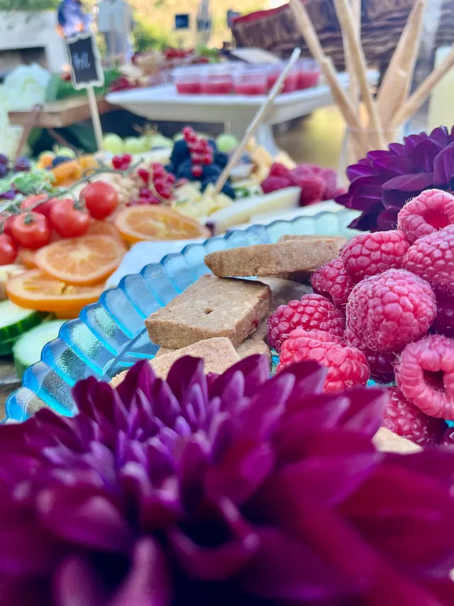 Close-up of a fruit and cheese board: raspberries, orange slices and shortbread beside deep purple dahlias