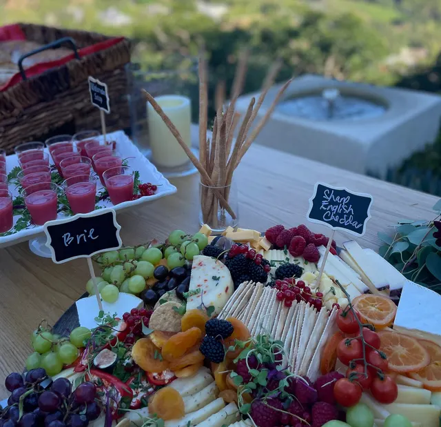 An outdoor grazing table with a sharp English cheddar board, breadsticks, a candle and shot glasses of chilled soup