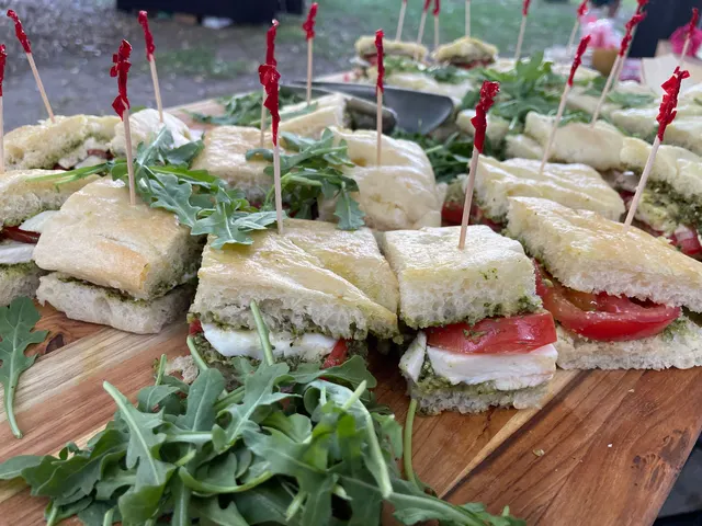 Caprese sandwich bites of mozzarella, tomato, pesto and arugula on focaccia, each held with a red-tipped pick