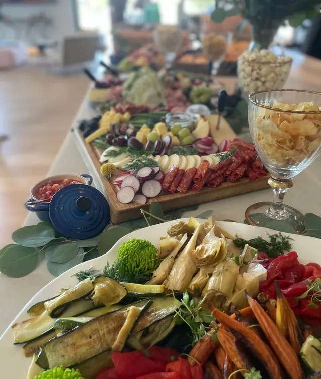 A platter of roasted zucchini, artichokes, carrots and peppers in front of a charcuterie board and popcorn