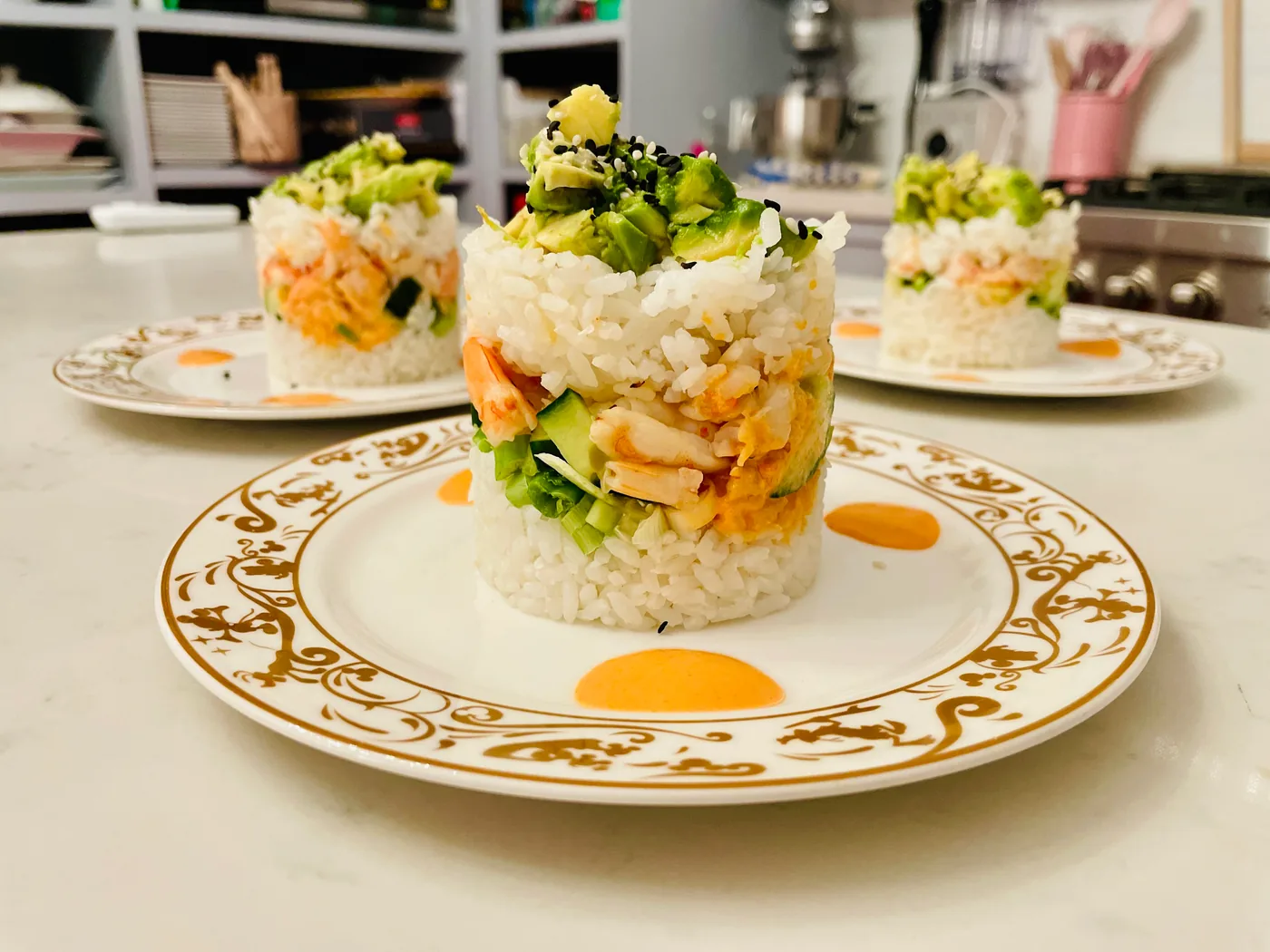Layered rice stacks with salmon and avocado plated on gold-rimmed china